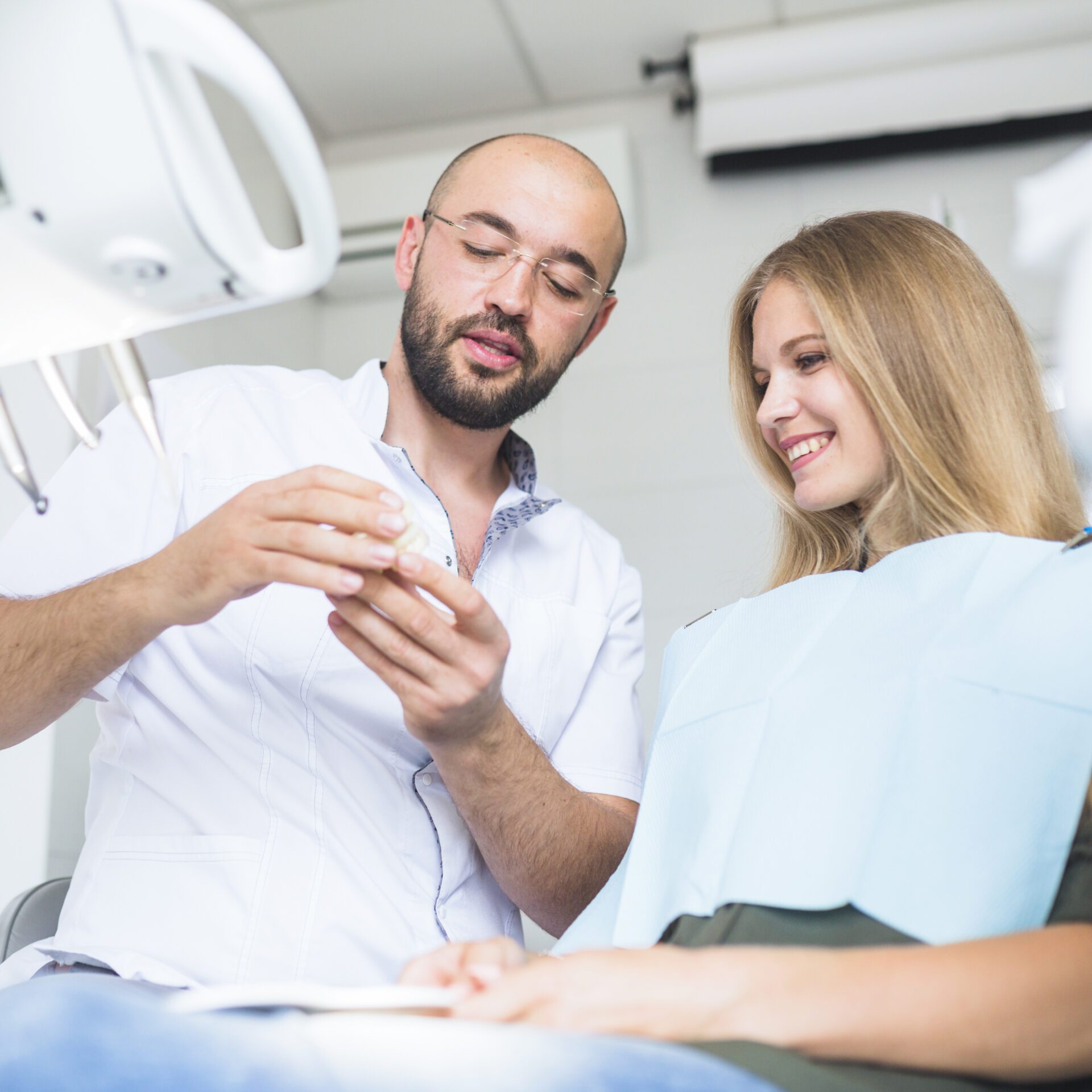 male-dentist-showing-dental-jaw-happy-female-patient